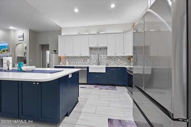 kitchen featuring blue cabinetry, light countertops, appliances with stainless steel finishes, white cabinets, and a sink