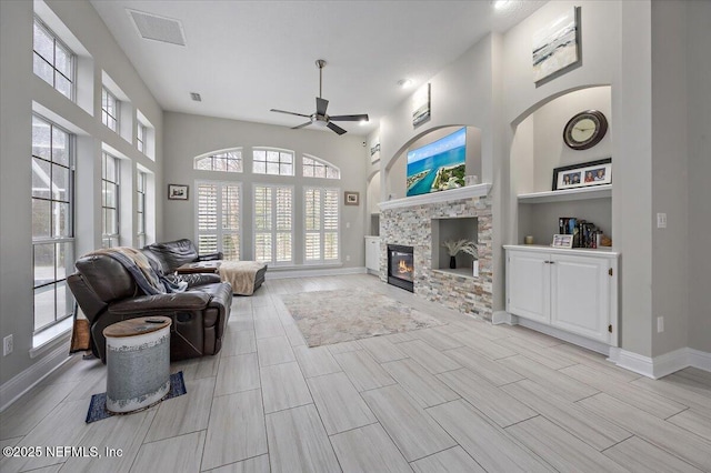 living room with ceiling fan, a glass covered fireplace, visible vents, and baseboards