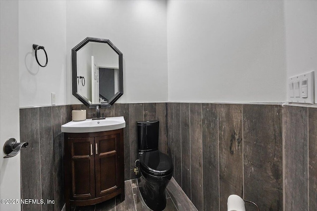 half bathroom with a wainscoted wall, toilet, vanity, and wooden walls