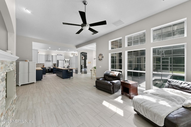 living room with ceiling fan, a stone fireplace, and visible vents