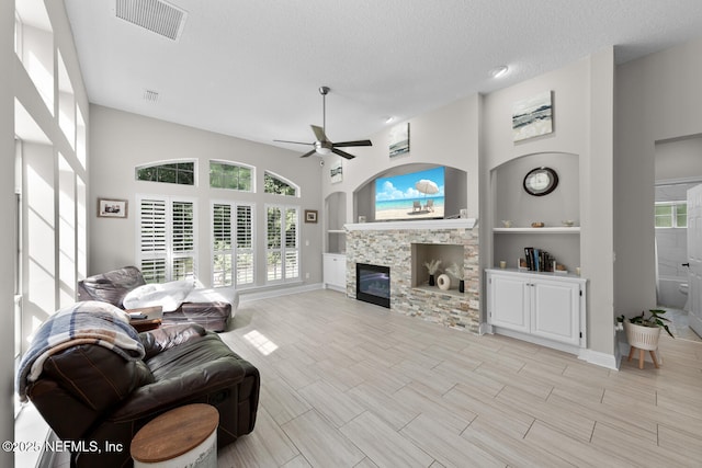 living room with a textured ceiling, built in shelves, a glass covered fireplace, and a wealth of natural light