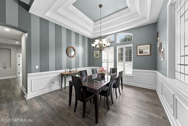 dining room with a chandelier, a decorative wall, a wainscoted wall, dark wood finished floors, and a raised ceiling