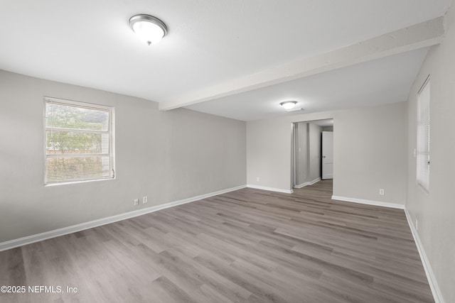 empty room with baseboards, beam ceiling, and wood finished floors