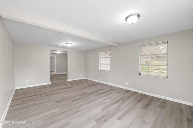 spare room with light wood-type flooring, beamed ceiling, and baseboards