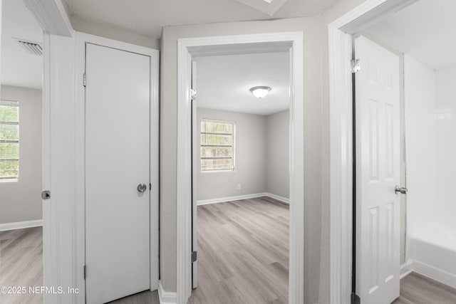 hallway featuring light wood finished floors, visible vents, and baseboards