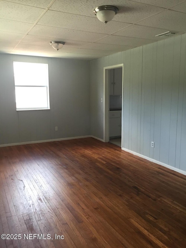 unfurnished room featuring visible vents, baseboards, a drop ceiling, and dark wood-style flooring