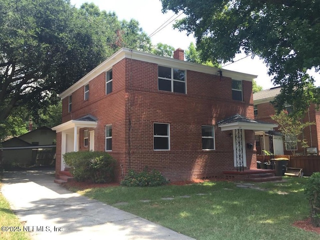 view of front of home with a front yard, a chimney, and brick siding