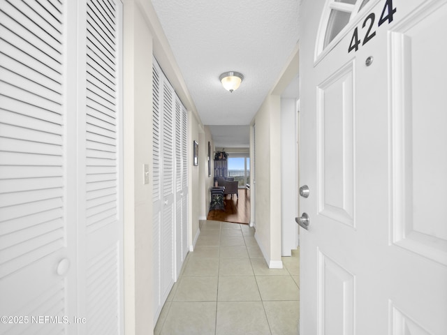hallway featuring light tile patterned floors, a textured ceiling, and baseboards