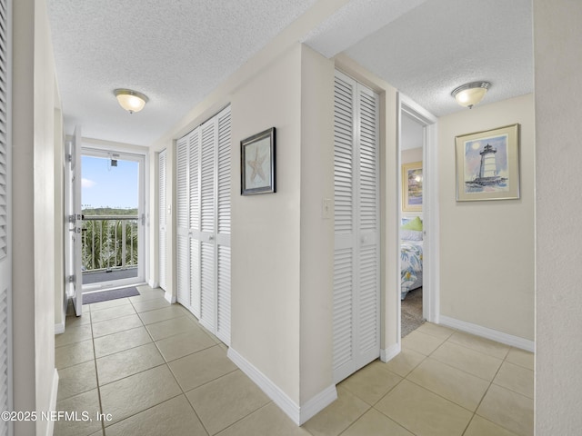 corridor featuring light tile patterned floors, baseboards, and a textured ceiling
