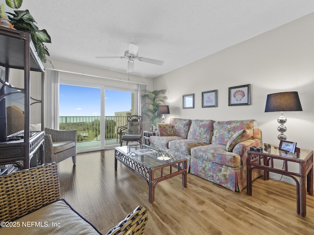 living area with ceiling fan, a textured ceiling, and wood finished floors