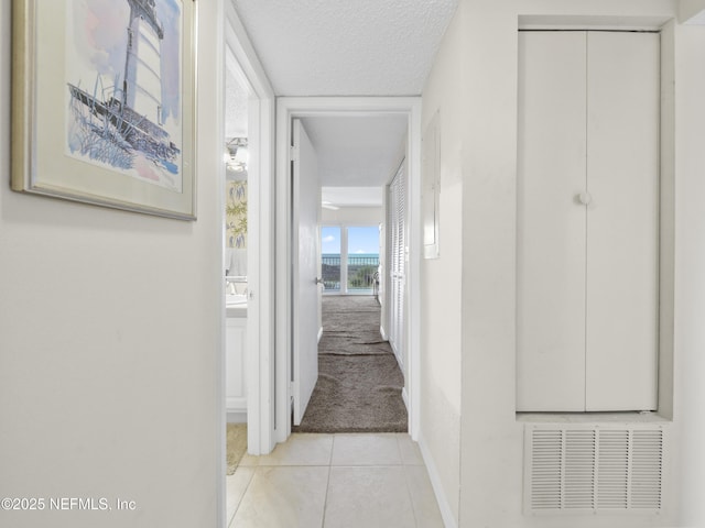 hall featuring visible vents, baseboards, light colored carpet, light tile patterned flooring, and a textured ceiling