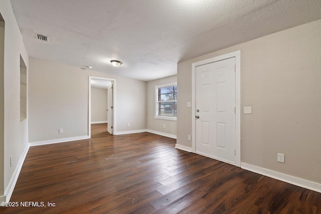 empty room with visible vents, a textured ceiling, baseboards, and dark wood-style flooring