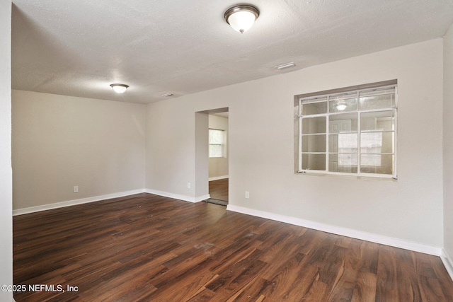 empty room featuring dark wood-style floors, a textured ceiling, and baseboards