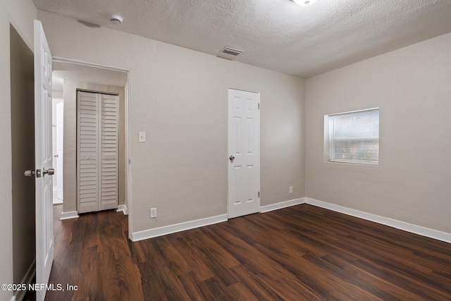 unfurnished bedroom featuring baseboards, a textured ceiling, visible vents, and wood finished floors