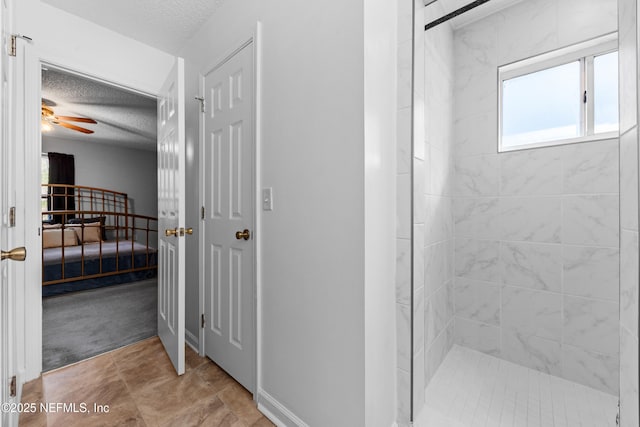 bathroom featuring a ceiling fan, a textured ceiling, ensuite bath, tiled shower, and baseboards