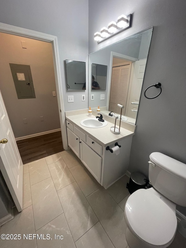 bathroom featuring baseboards, electric panel, vanity, and toilet