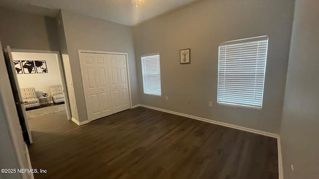 unfurnished bedroom with a closet, dark wood finished floors, and baseboards