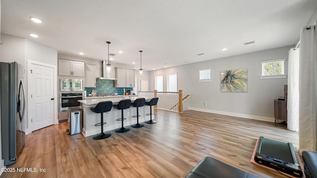 kitchen with a kitchen island with sink, light countertops, appliances with stainless steel finishes, a kitchen bar, and decorative light fixtures