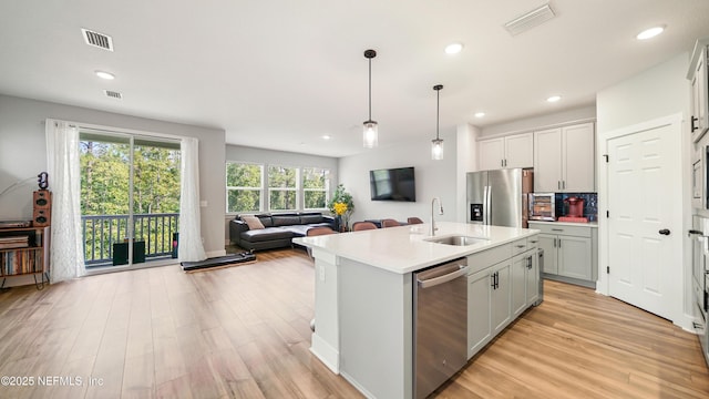 kitchen with a kitchen island with sink, a sink, open floor plan, light countertops, and appliances with stainless steel finishes