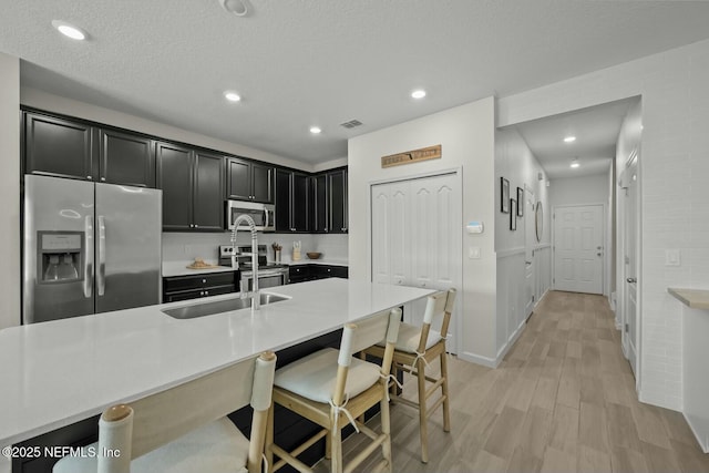 kitchen featuring light countertops, appliances with stainless steel finishes, light wood-style floors, dark cabinets, and a kitchen breakfast bar