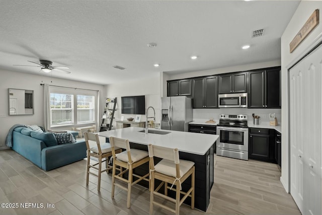 kitchen featuring visible vents, appliances with stainless steel finishes, open floor plan, dark cabinetry, and a sink