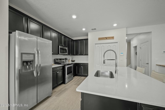 kitchen with light countertops, dark cabinetry, stainless steel appliances, wood finish floors, and a sink