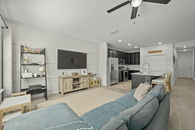 living area with ceiling fan, a textured ceiling, light wood-style flooring, recessed lighting, and visible vents