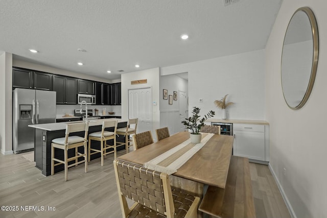 dining room with a textured ceiling, wine cooler, light wood-style flooring, and recessed lighting