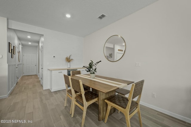 dining area featuring light wood finished floors, baseboards, visible vents, a textured ceiling, and recessed lighting