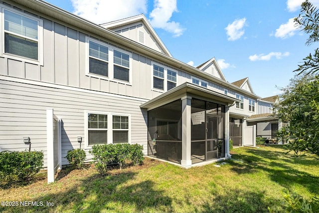 rear view of property featuring board and batten siding, a sunroom, a yard, and a balcony