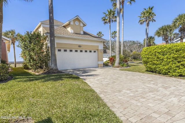 180 Kingston Dr, Saint Augustine, FL 32084 - view of home's exterior with a lawn, a garage, stucco siding, decorative driveway, and roof with shingles