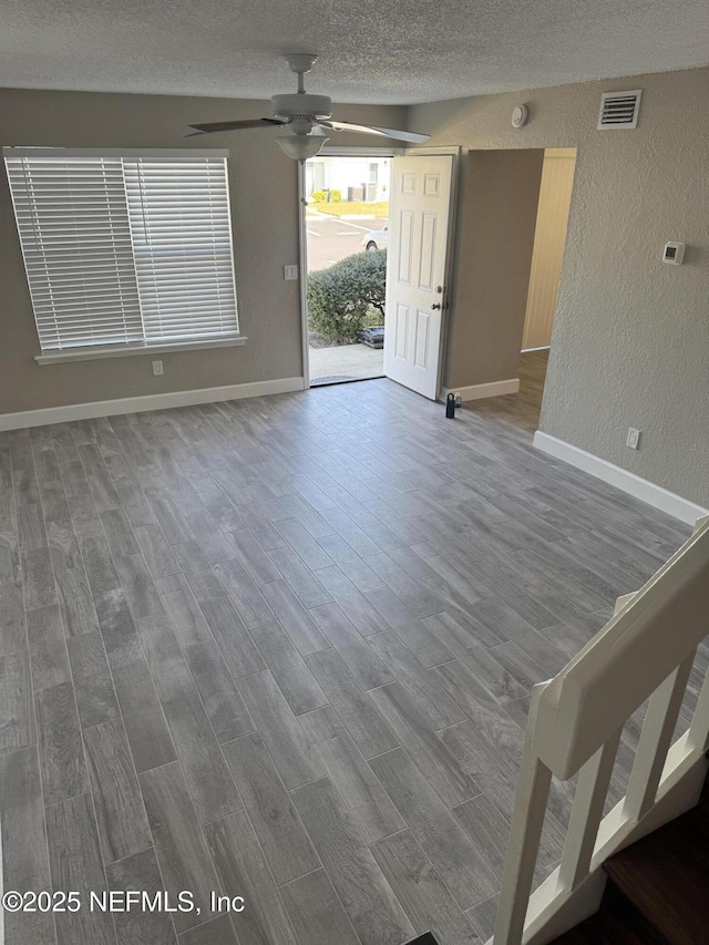 unfurnished living room featuring visible vents, a textured wall, ceiling fan, wood finished floors, and a textured ceiling