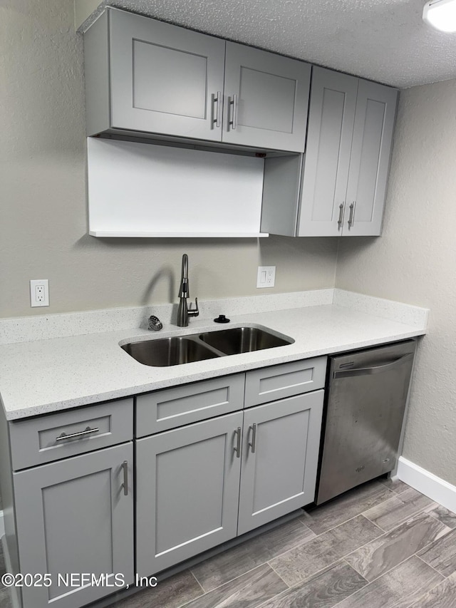 kitchen with a sink, gray cabinets, stainless steel dishwasher, and wood finish floors