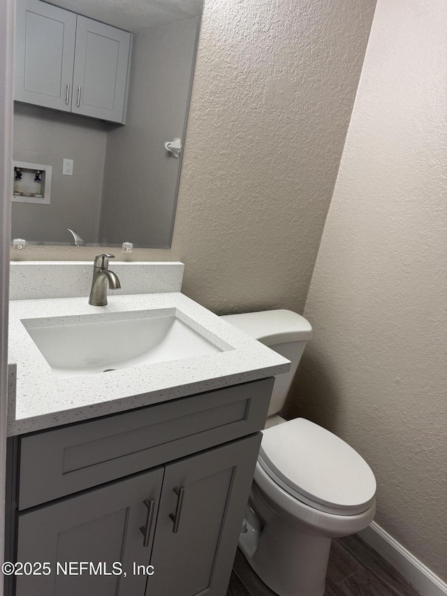 bathroom featuring toilet, a textured wall, wood finished floors, and vanity