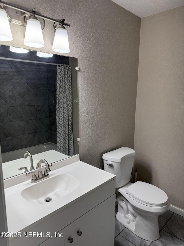 bathroom featuring a textured wall, vanity, toilet, and baseboards