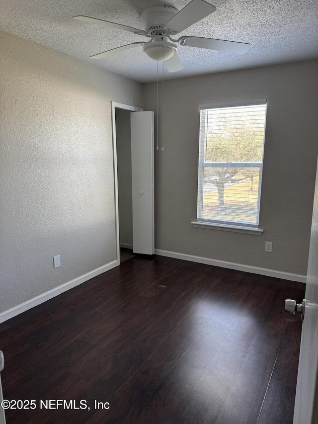 unfurnished room with dark wood finished floors, a textured ceiling, and baseboards