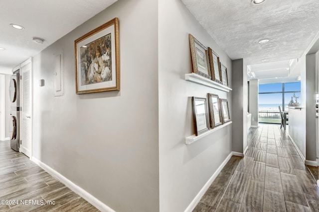 hall featuring baseboards, wood tiled floor, expansive windows, a textured ceiling, and stacked washing maching and dryer