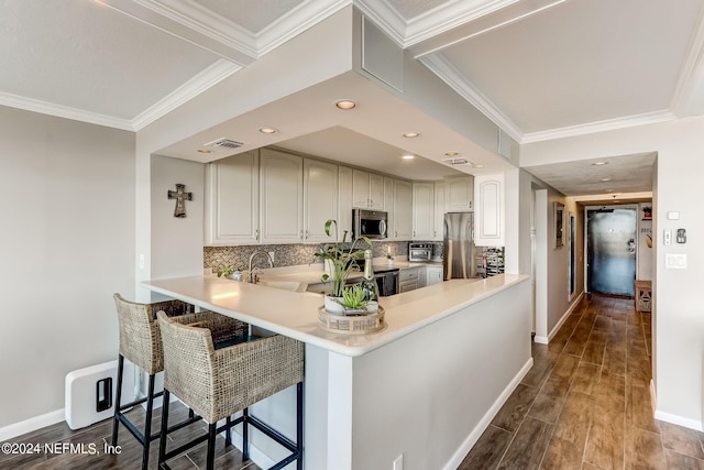 kitchen featuring a breakfast bar, light countertops, decorative backsplash, appliances with stainless steel finishes, and a peninsula