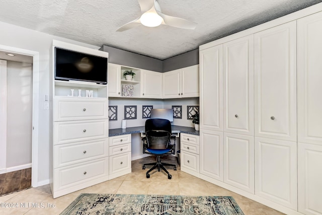 office featuring a textured ceiling, light tile patterned floors, a ceiling fan, baseboards, and built in desk