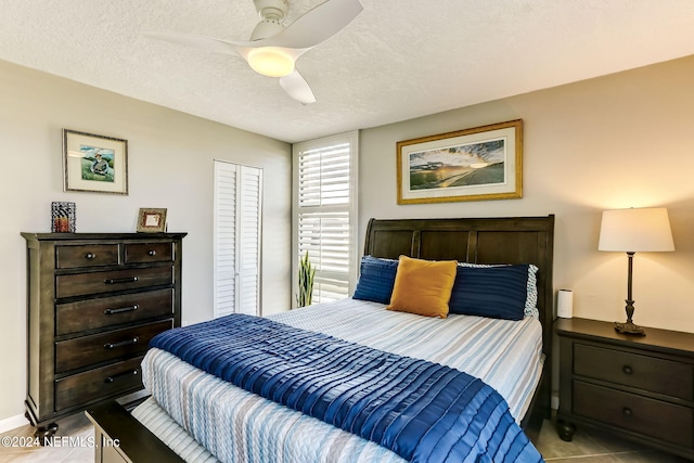 bedroom featuring a textured ceiling, light tile patterned floors, a closet, and a ceiling fan