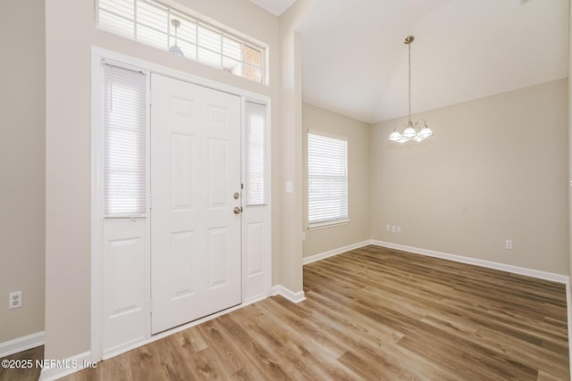 entrance foyer featuring lofted ceiling, baseboards, a chandelier, and wood finished floors