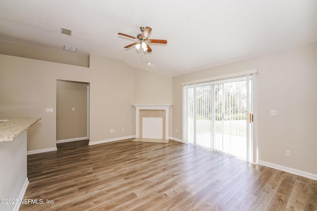 unfurnished living room featuring lofted ceiling, a tiled fireplace, a ceiling fan, wood finished floors, and baseboards