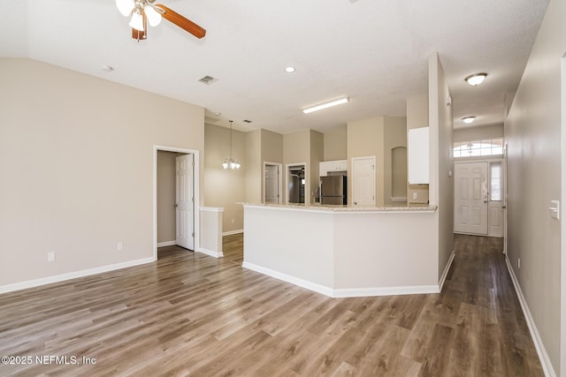 kitchen with dark wood-style floors, freestanding refrigerator, white cabinetry, and a peninsula