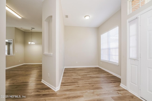 hallway featuring visible vents, baseboards, arched walkways, wood finished floors, and a notable chandelier