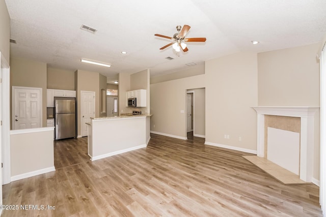 kitchen featuring light wood finished floors, stainless steel appliances, lofted ceiling, white cabinets, and baseboards