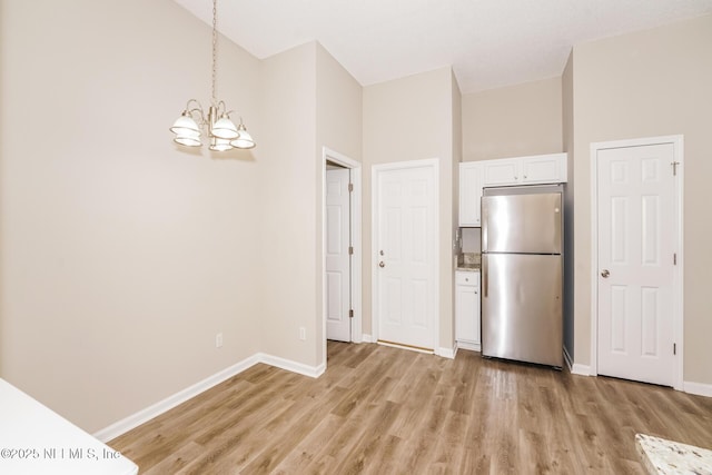 kitchen featuring decorative light fixtures, light wood-type flooring, freestanding refrigerator, and white cabinets