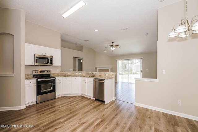 kitchen featuring a peninsula, white cabinets, open floor plan, appliances with stainless steel finishes, and decorative light fixtures