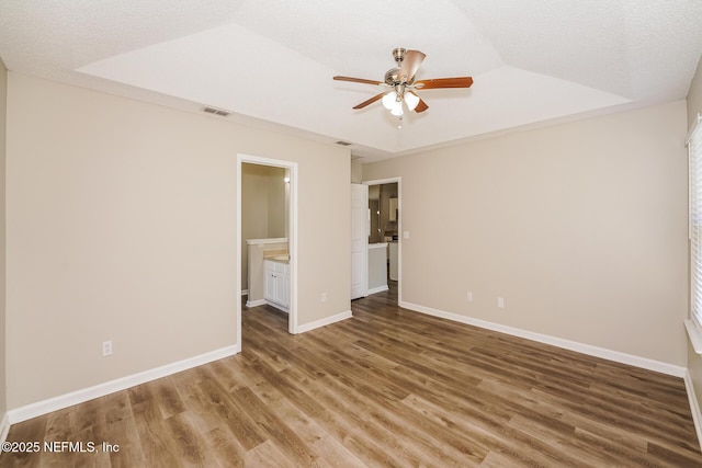 empty room with a textured ceiling, wood finished floors, visible vents, baseboards, and a raised ceiling