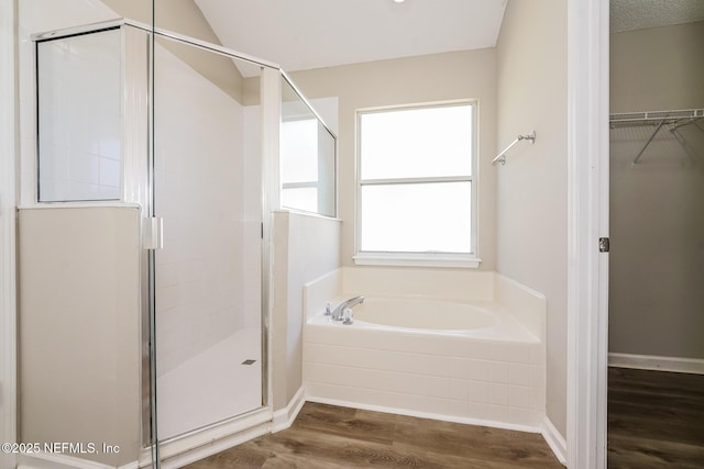 bathroom featuring a garden tub, a spacious closet, a stall shower, and wood finished floors