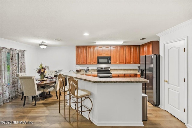 kitchen featuring visible vents, fridge with ice dispenser, stainless steel range with electric cooktop, light wood-style floors, and black microwave